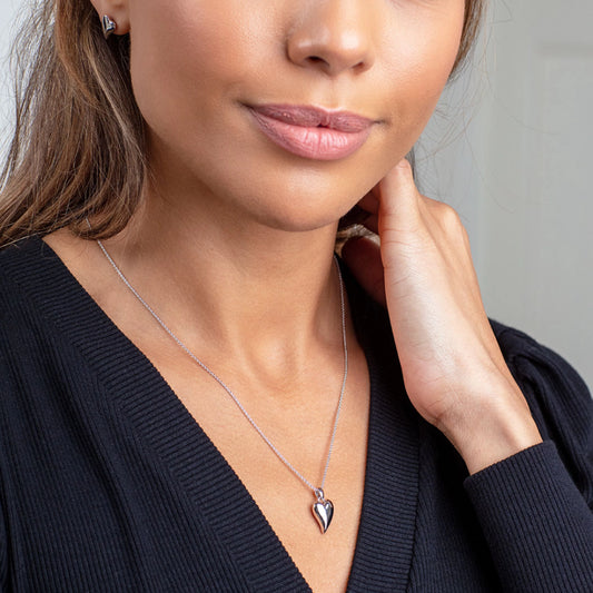 Model wearing a simple silver pendant on a chain in the shape of a heart