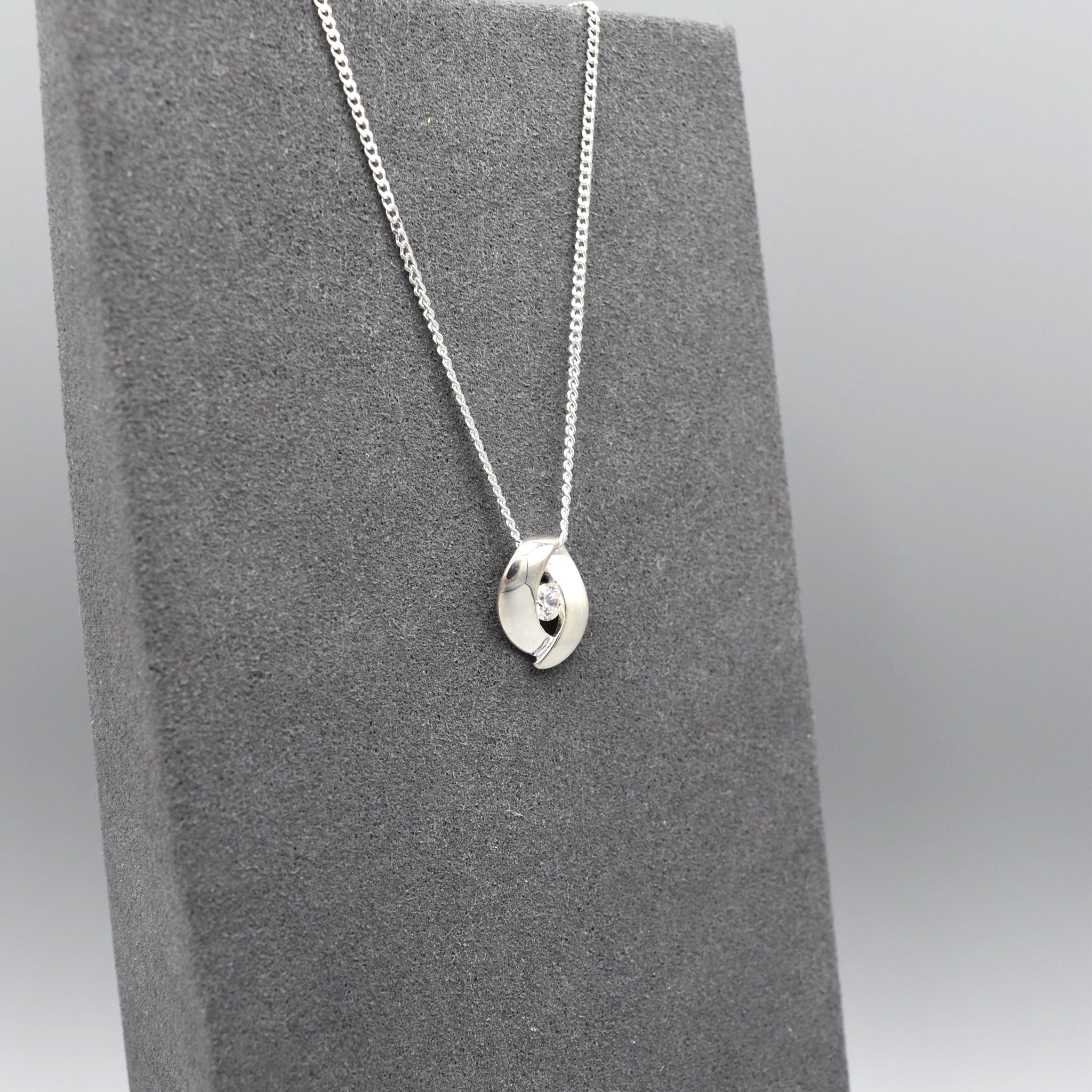 A double curve shaped silver pendant with CZ centre and matt texture