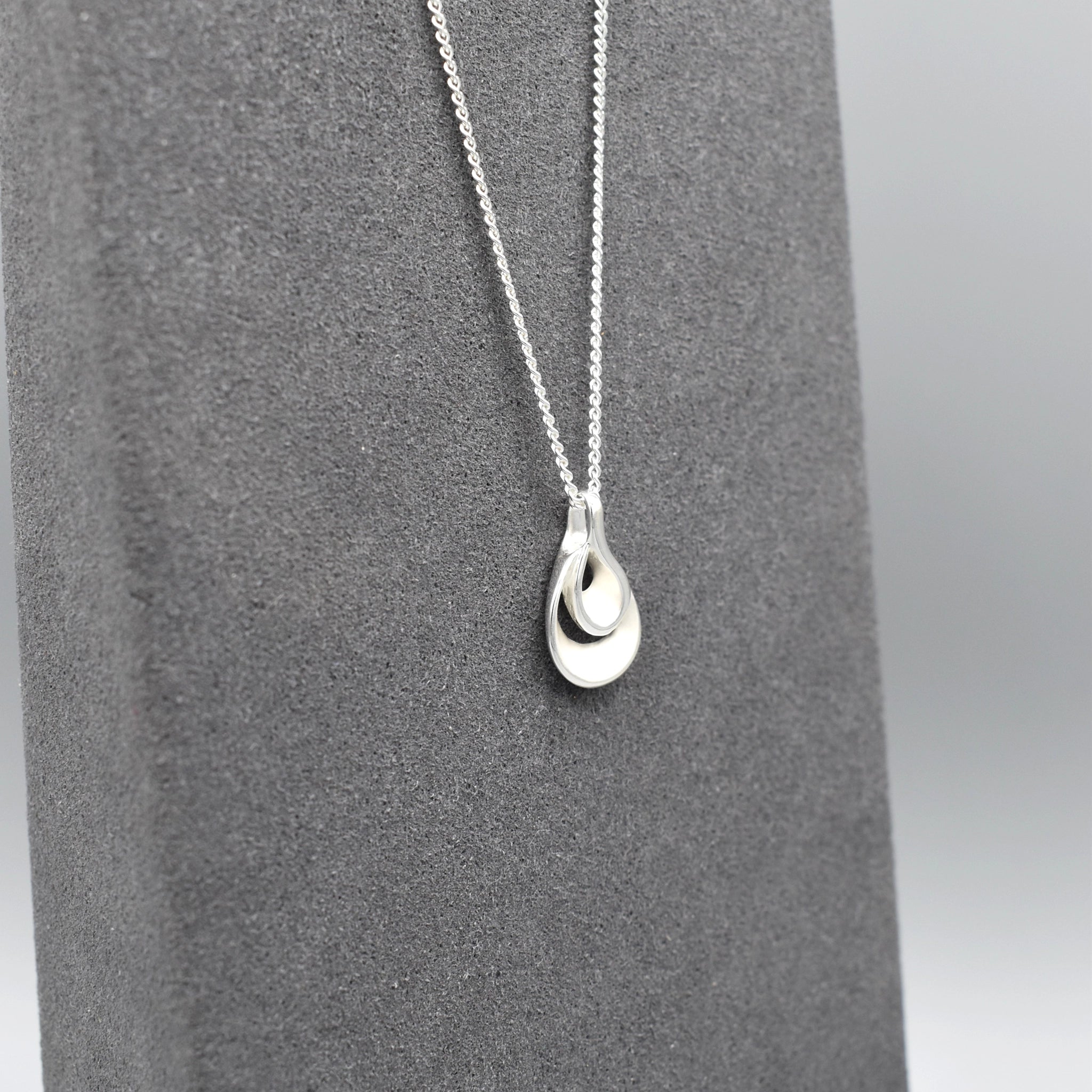 A double twisted teardrop shaped pendant with matt silver