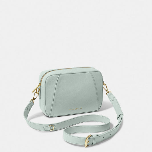 A light blue crossbody bag in a simple box shape with adjustable strap and gold hardware