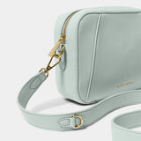 Detail of light blue crossbody bag in a simple box shape with adjustable strap and gold hardware