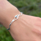 Model wearing a silver bracelet with two ripple links and a pendant of two ripples and a blue topaz