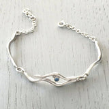 Silver bracelet with two ripple links and a pendant of two ripples and a blue topaz