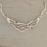 A silver necklet featuring 4 ripple patterns and two blue topaz stones