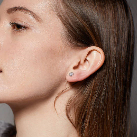 Model wearing a simple pair of round silver earrings set with micro-pavé CZ stones