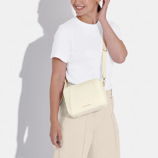 Model wearing ecru crossbody bag in a simple box shape with adjustable strap and gold hardware