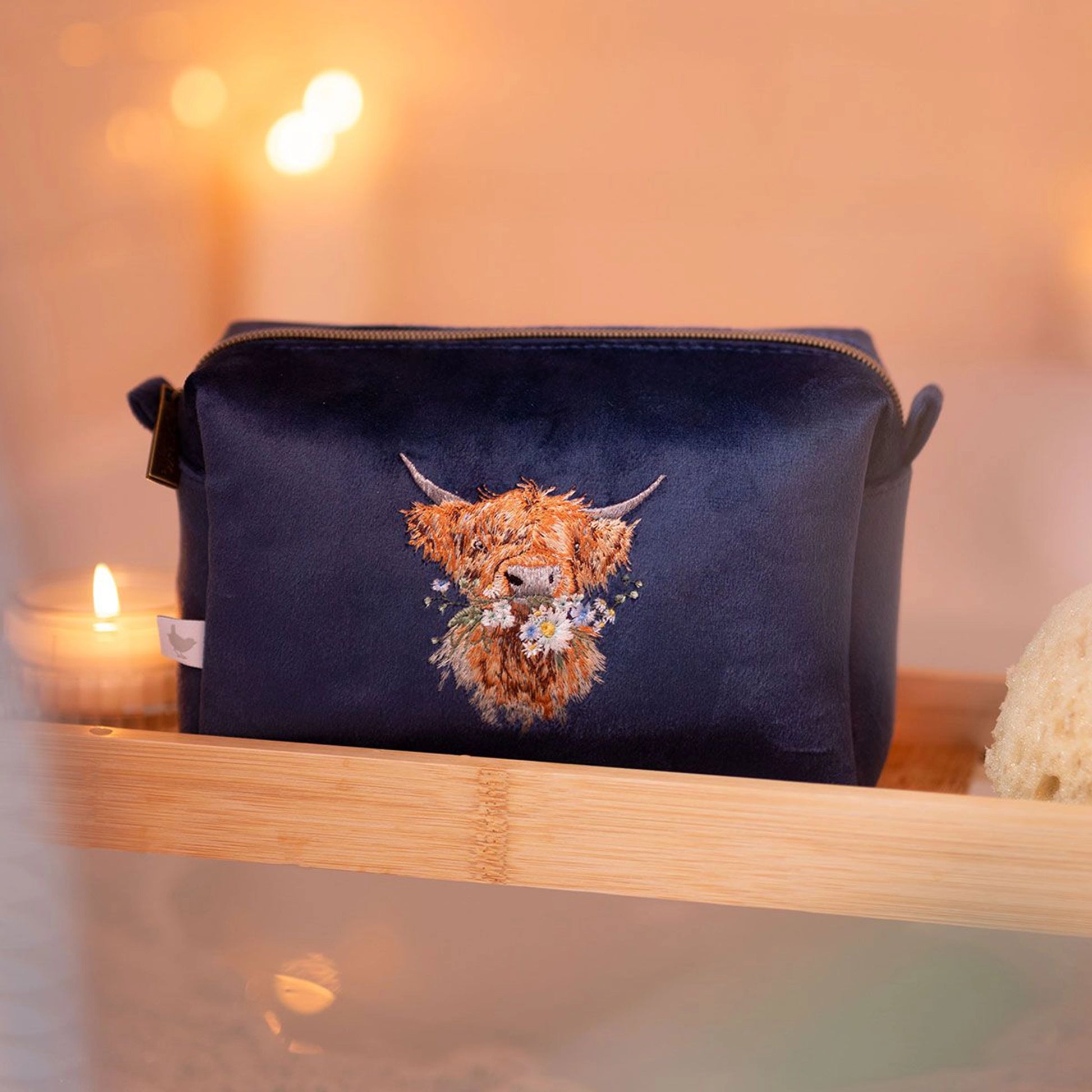 Navy blue make up bag with embroidered Highland cow design and zip top lifestyle