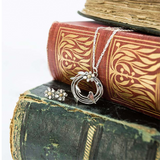 Round silver bird nest pendant with bird & leaf design and a flower with a gold centre on antique books