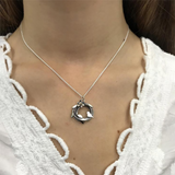 Model wearing round silver bird nest pendant with bird & leaf design and a flower with a gold centre on silver chain