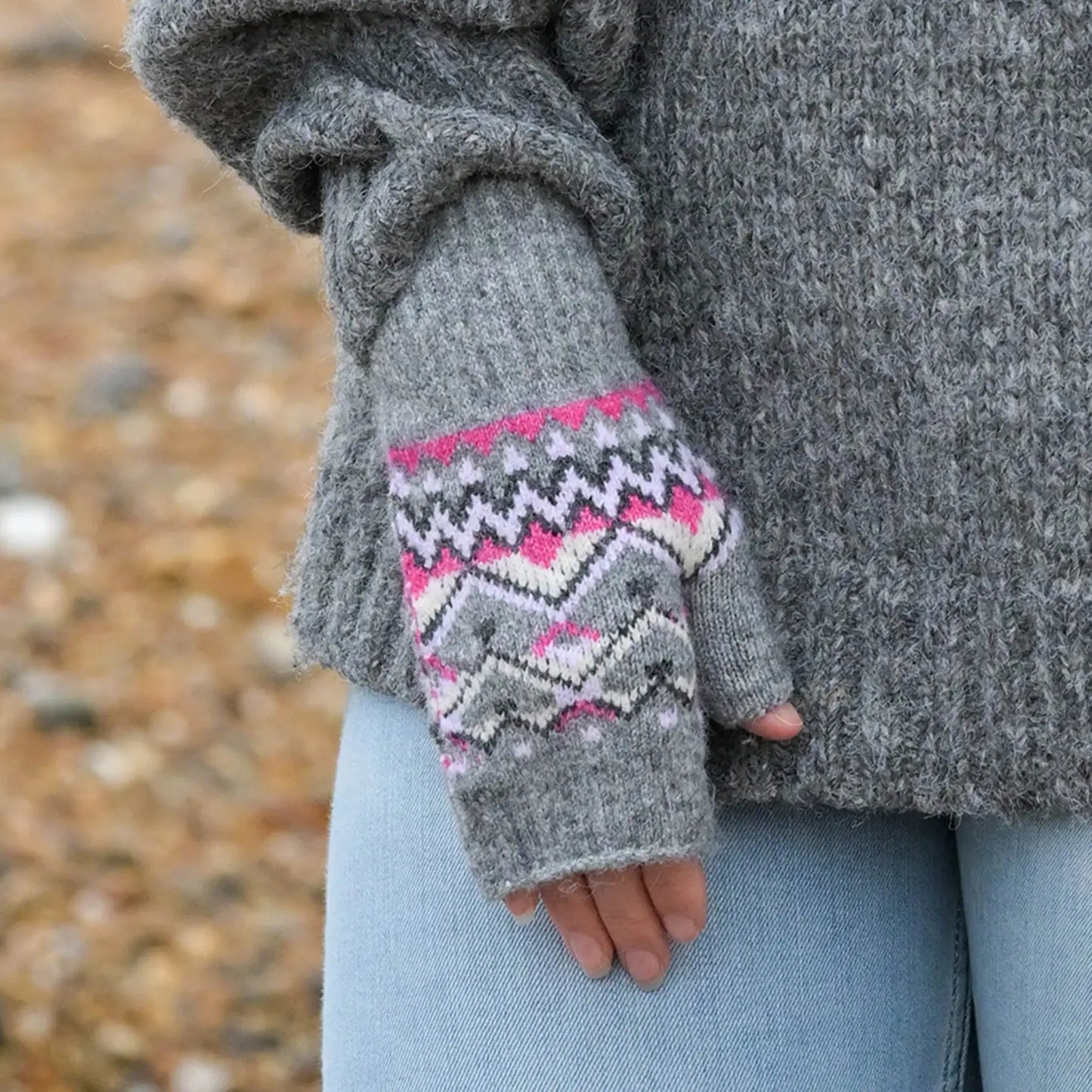 Model wearing pair of grey fingerless gloves with fair isle patterns in pink