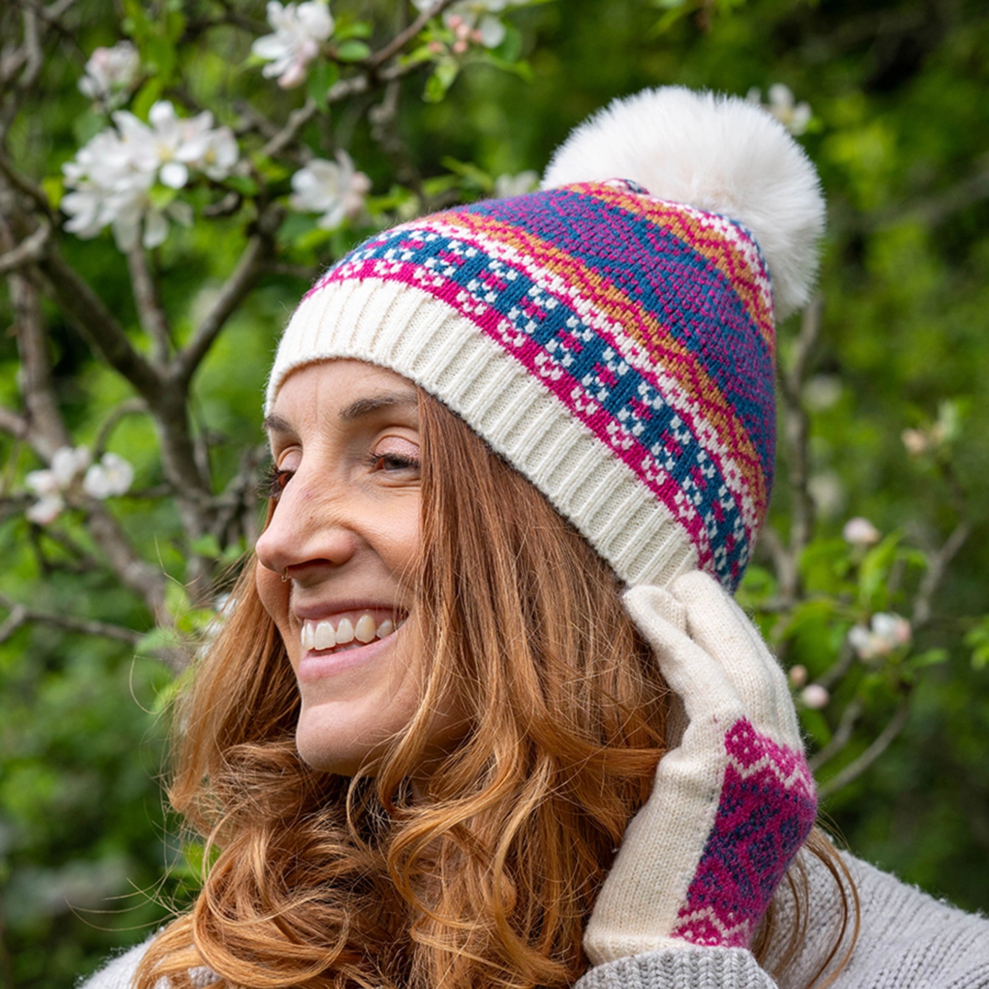 Model wearing knitted hat with fair isle pattern in cream, blue and pink and a faux fur pompom