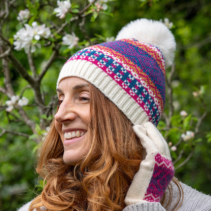 Model wearing knitted hat with fair isle pattern in cream, blue and pink and a faux fur pompom