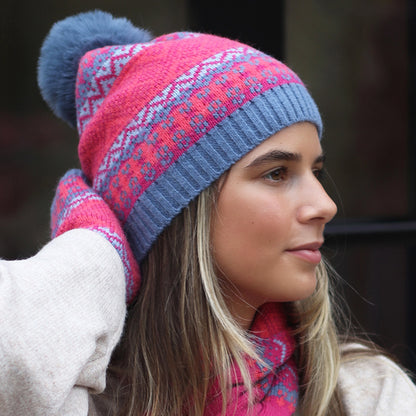 Model wearing knitted hat with fair isle pattern in blue, red and pink and a faux fur pompom