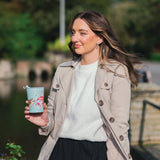 Model holding a blue thermal cup featuring a design of red toadstools with woodland creatures on them