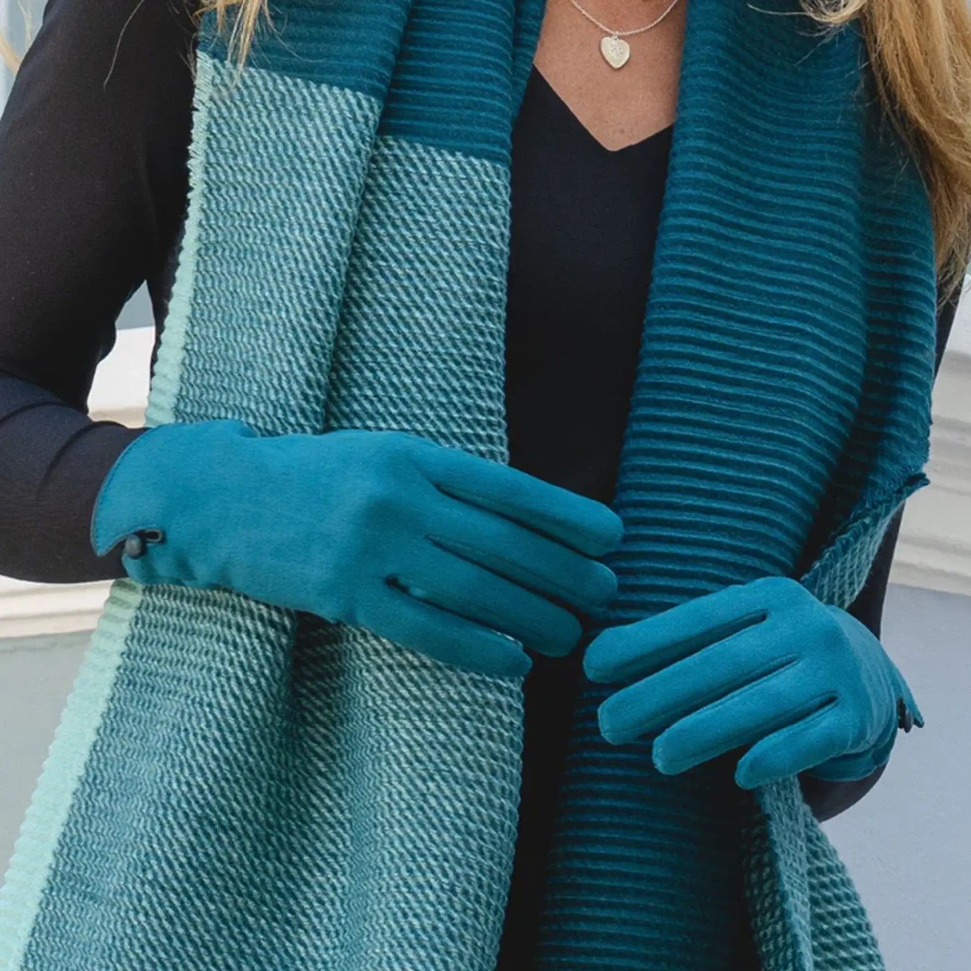 Model wearing teal suede gloves with single button detail on the cuff and touch screen finger