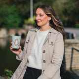 Model holding a green thermal mug featuring illustrations of cuddling cats