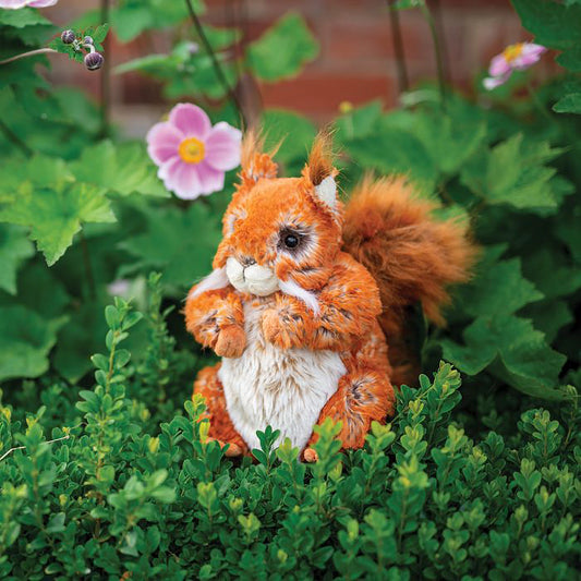 A stuffed squirrel plush toy with the Wrendale logo embroidered on the bottom of its foot posed in a garden