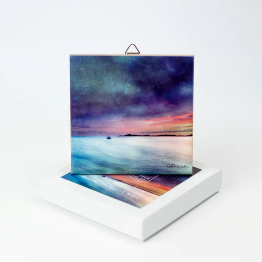 A ceramic tile featuring a water and sky scene painting by Cath Waters with packaging
