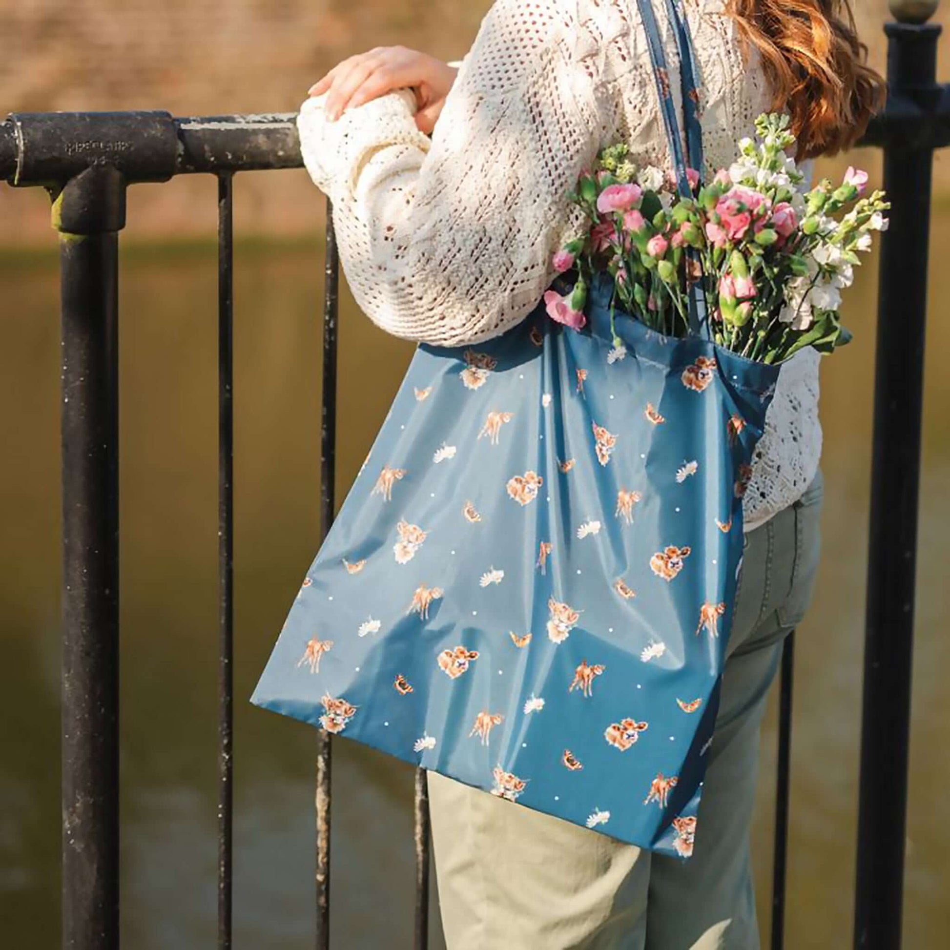 Model wearing blue shopping tote bag with Highland Cow pattern