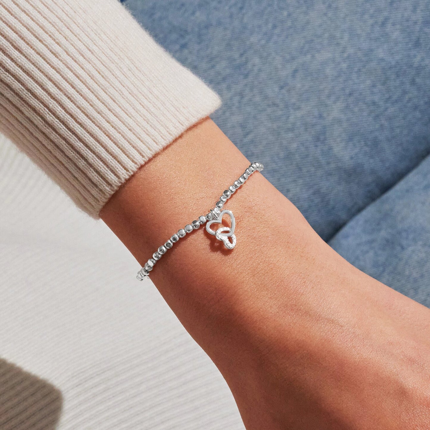 Model wearing silver stretch beaded bracelet with two interlocked hearts