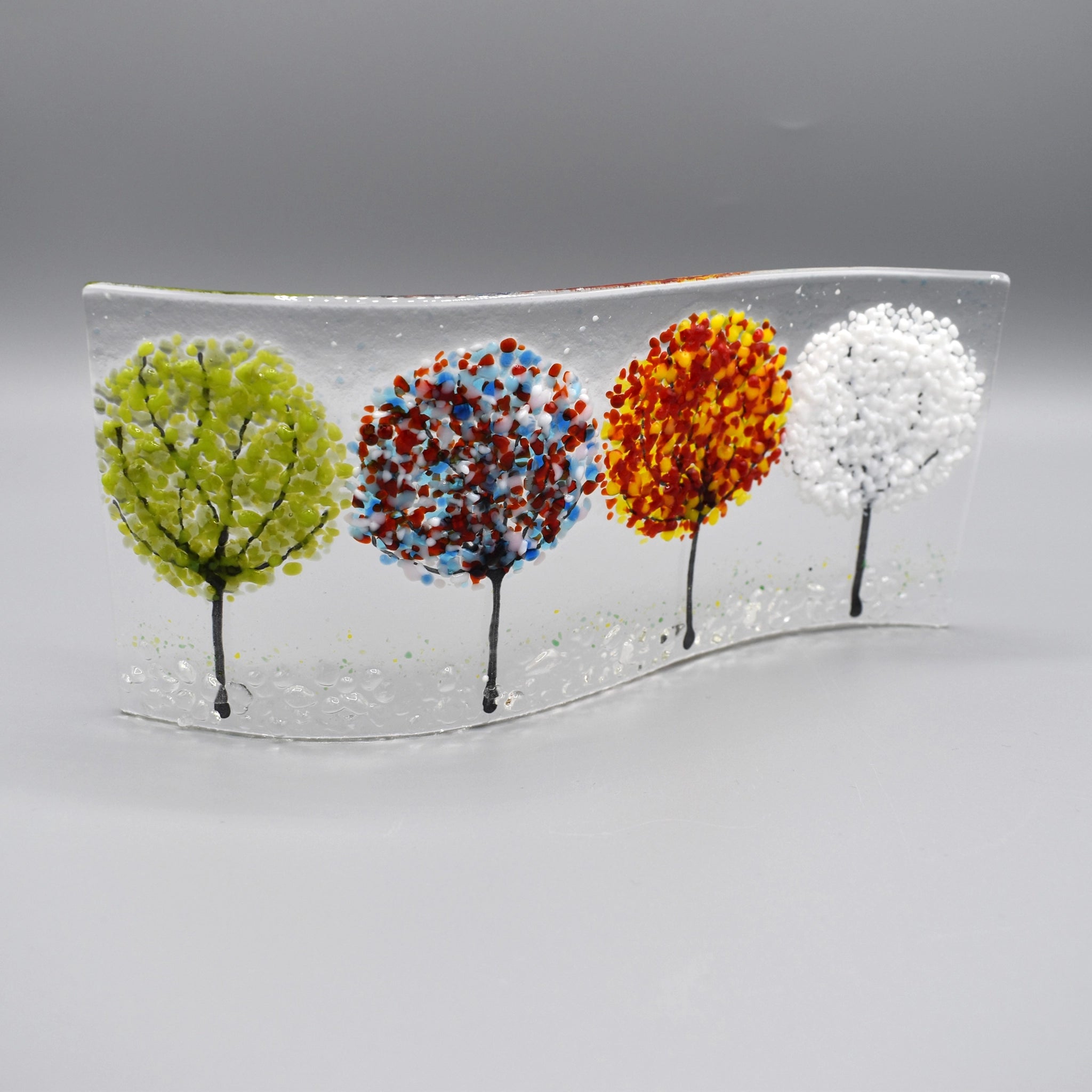 A glass curve sculpture with four trees in different seasonal colours