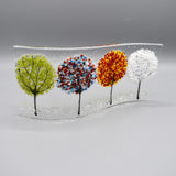 A glass curve sculpture with four trees in different seasonal colours