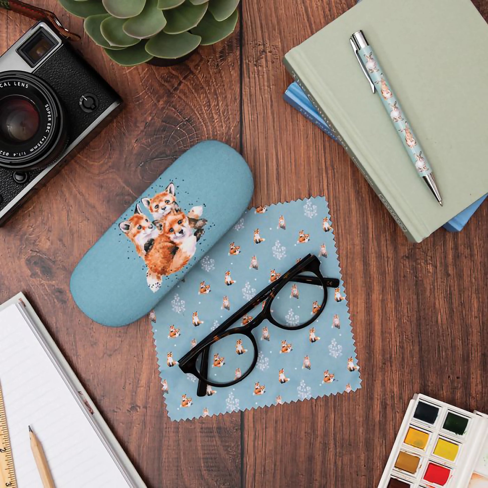 Light blue glasses case with design of three cuddling fox cubs and a polishing cloth with fox pattern 