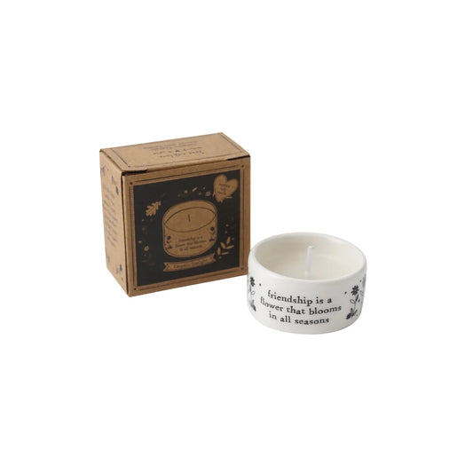 A small white ceramic tealight holder featuring a phrase and floral design