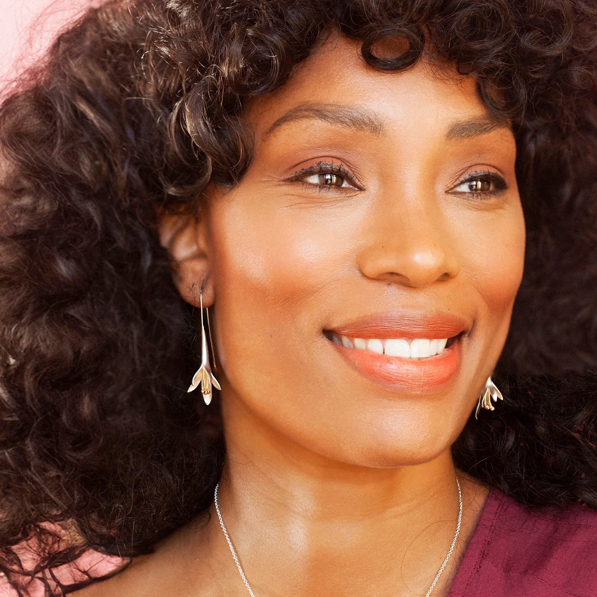 Model wearing satin silver fuchsia shaped earrings with gold stamen and long hooks