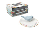 Small white oval dish with roses painted along one edge and a ceramic blue bird on the opposite side
