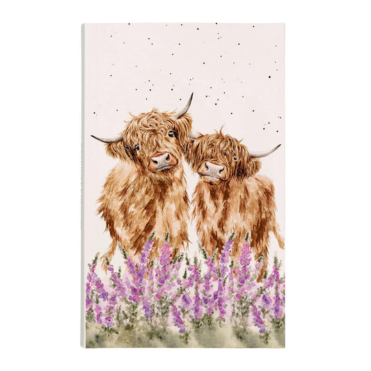 A pink notebook with two Highland cows in a field of pink flowers on the cover