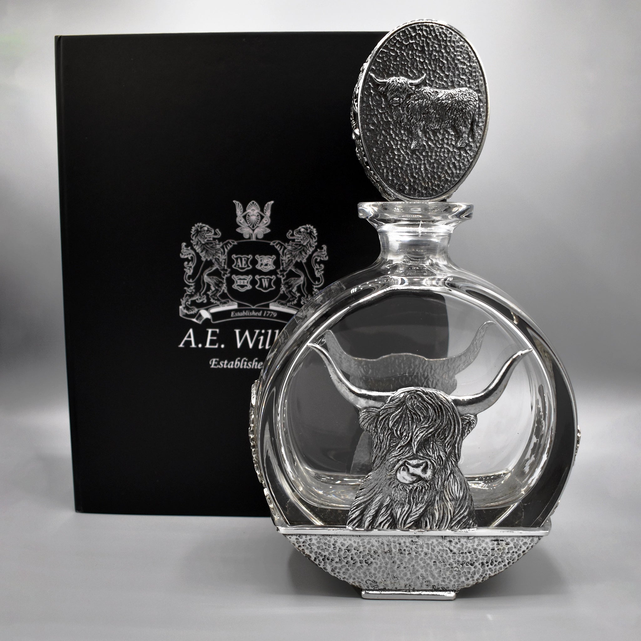 A glass decanter with pewter Highland cow oval stopper and Highland cow design on the base by black packaging box