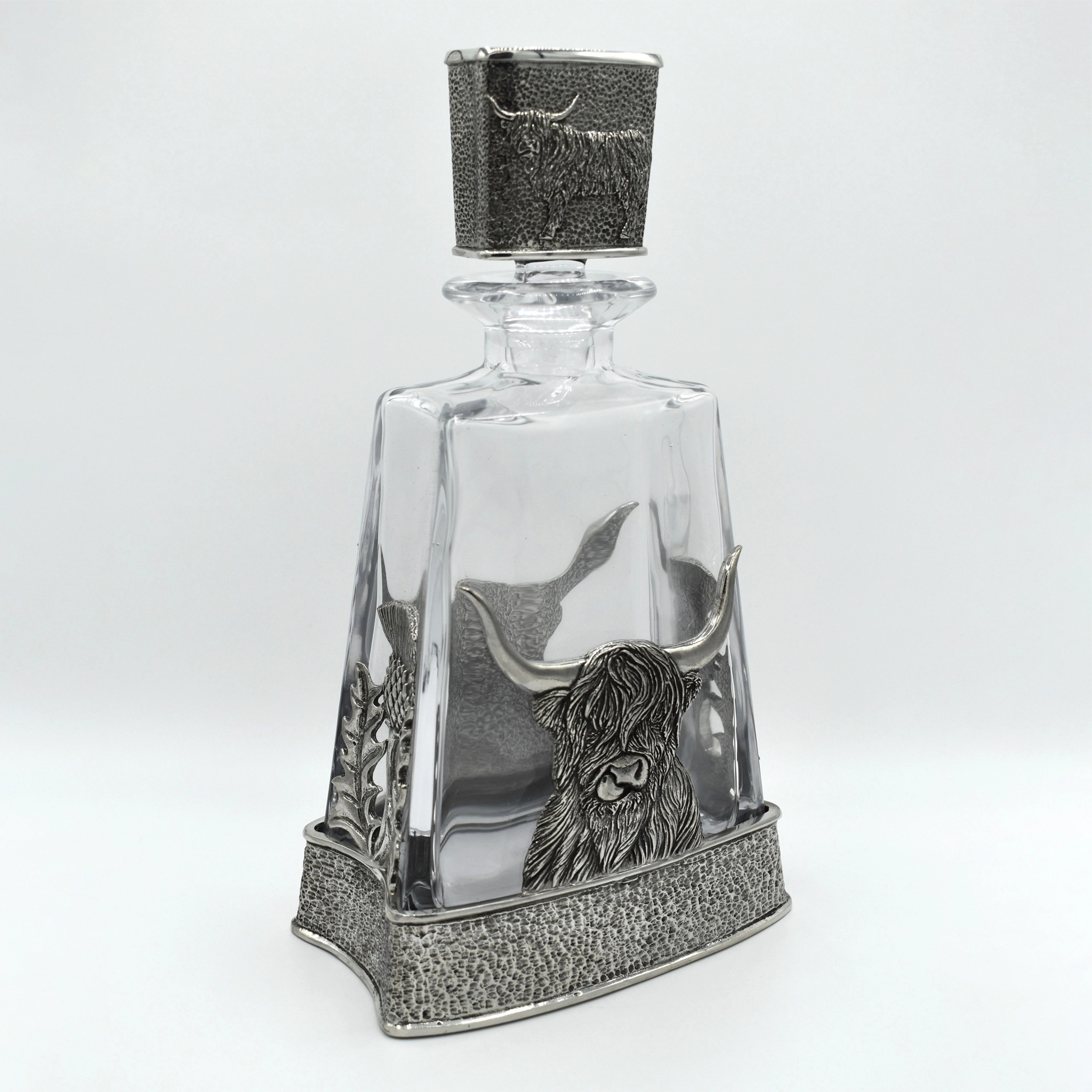 A glass decanter with pewter base featuring a Highland cow, and matching pewter stopper side