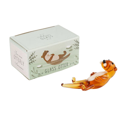 Glass otter figurine swimming on its back next to a matching gift box