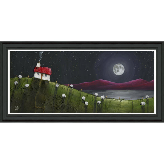 A rectangular framed print of a hill at night with little sheep and a house