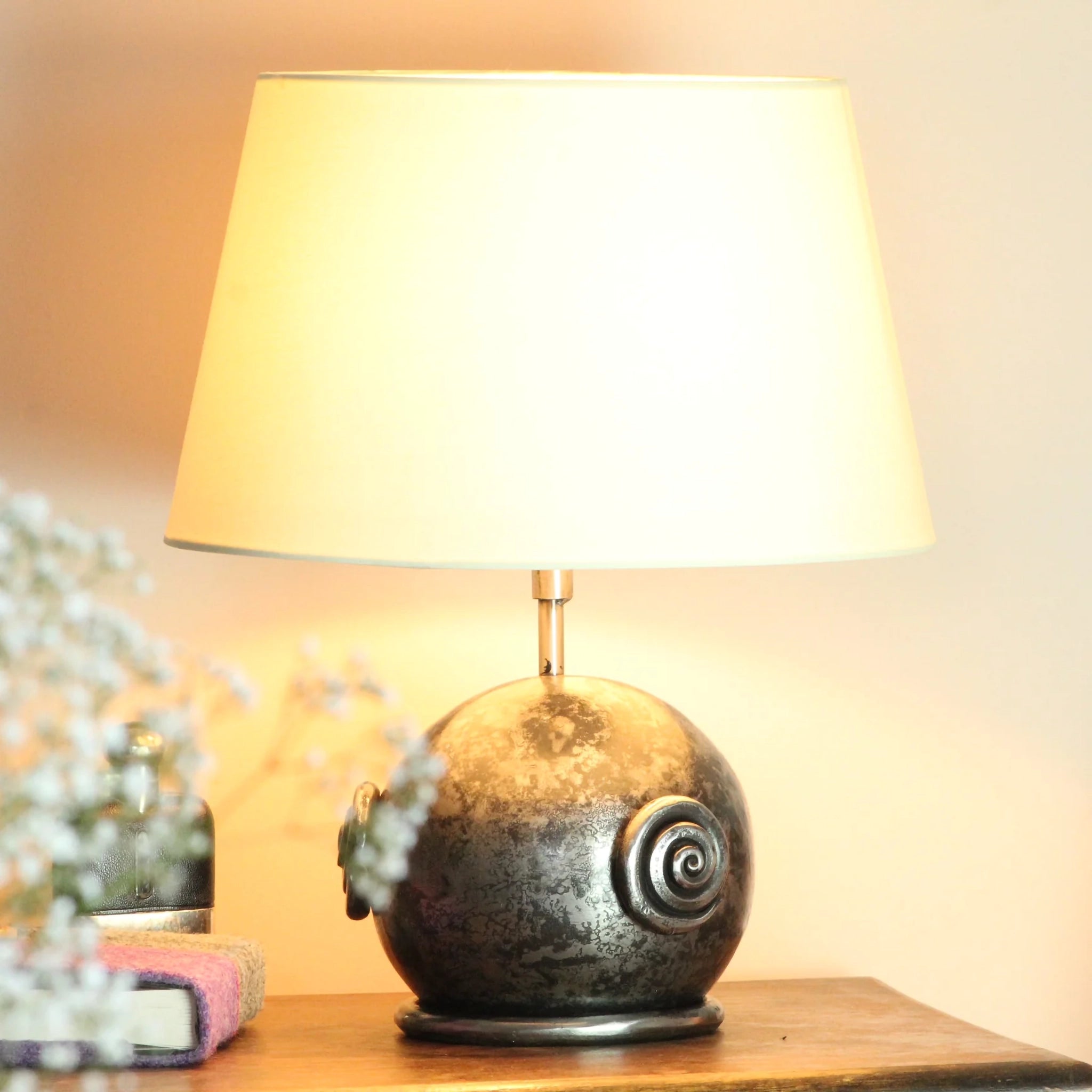 A globe shaped table lamp in a dark polished steel with a cream shallow drum shade and scroll design