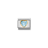 A Nomination charm link featuring a light blue faceted heart shaped cubic zirconia stone with gold surround