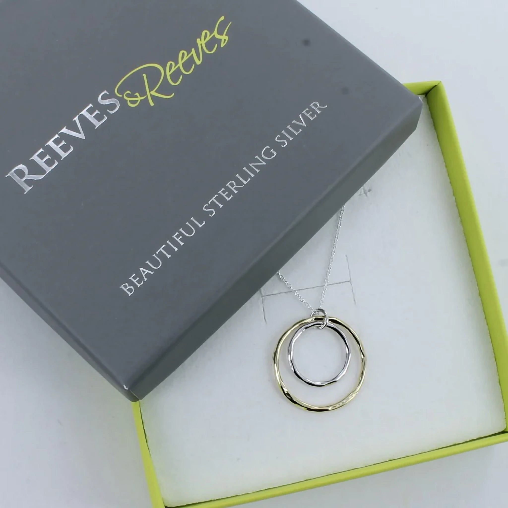 A necklace featuring a small silver hoop inside a larger gold hoop with irregular texturing in branded box