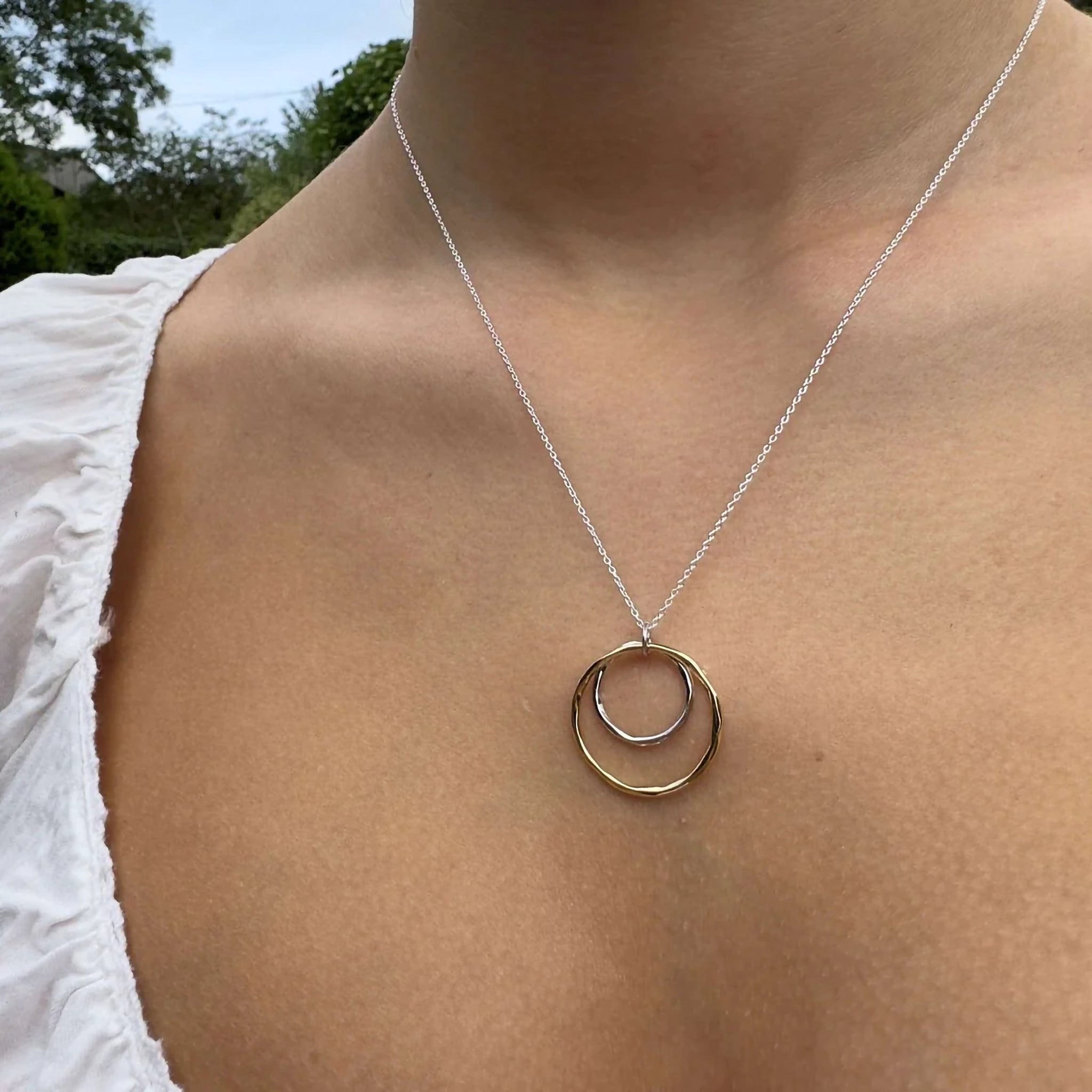 Model wearing a necklace featuring a small silver hoop inside a larger gold hoop with irregular texturing