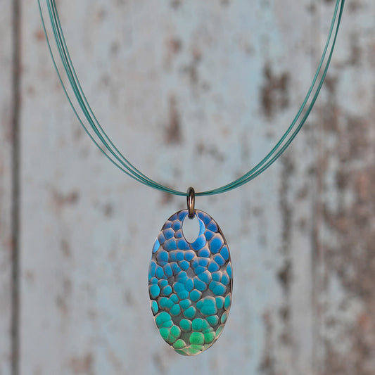 An oval pendant with green and blue ripple design pattern