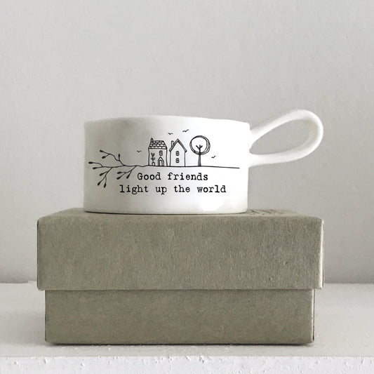 A white handled tealight holder featuring two little houses illustration and a quote on a box