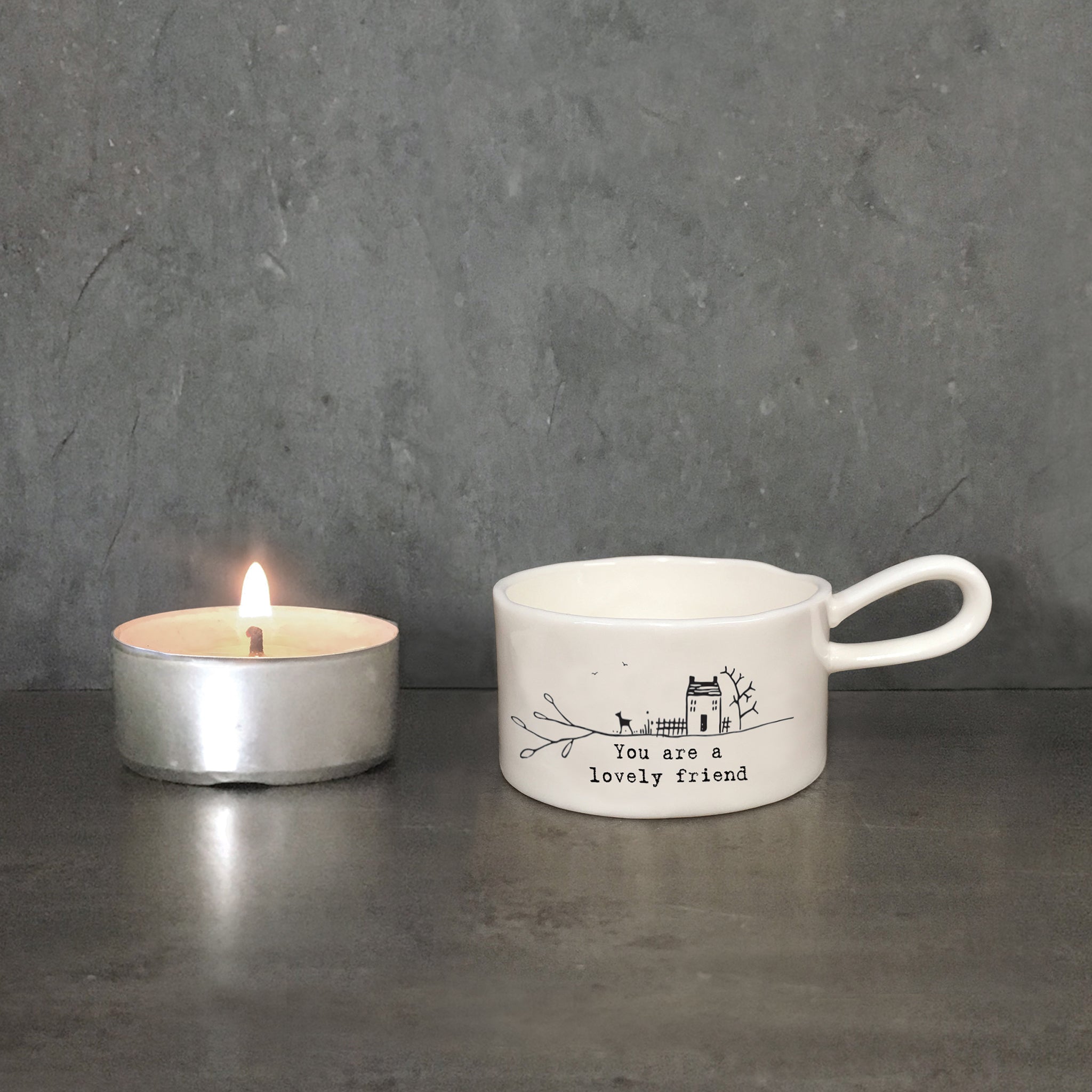 A white handled tealight holder featuring a little house & dog illustration and a quote with candle