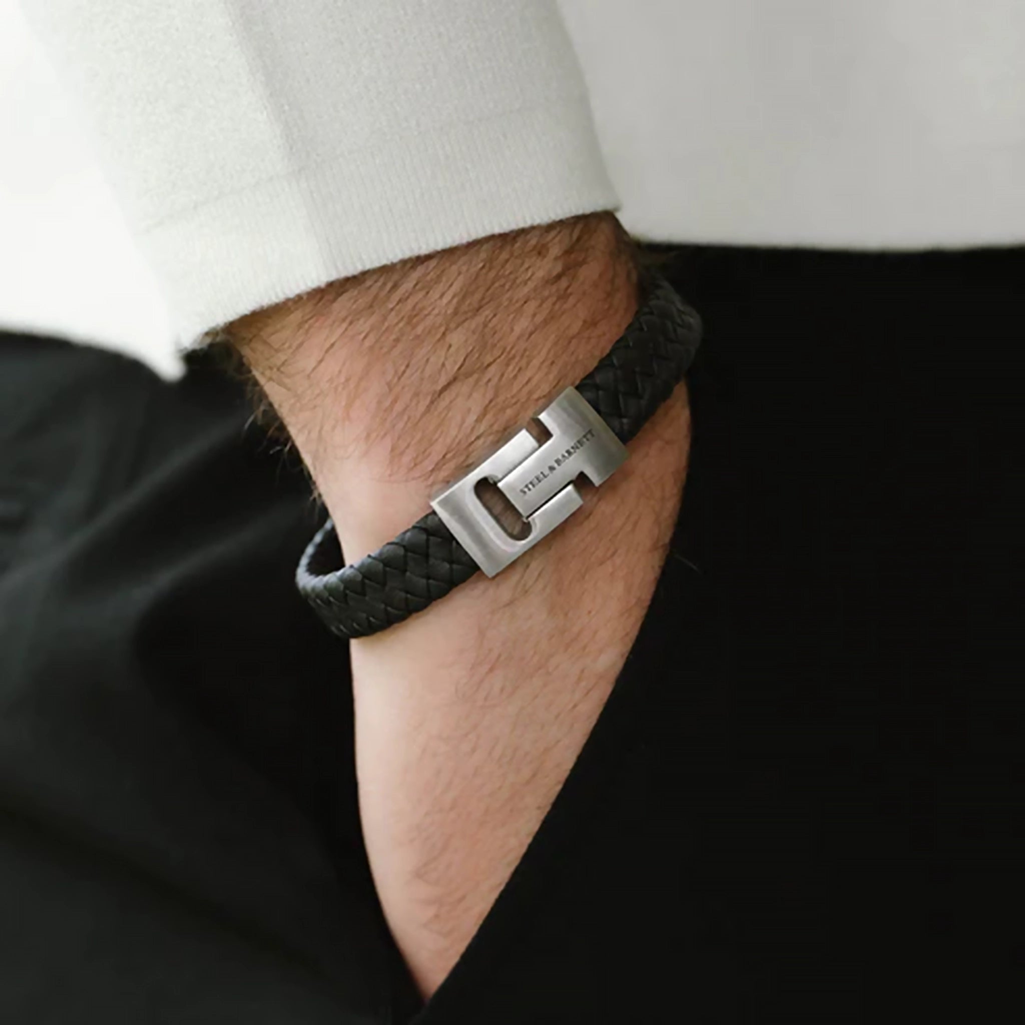 Model wearing a braided black leather bracelet with stainless steel bar detail and chunky slider clasp