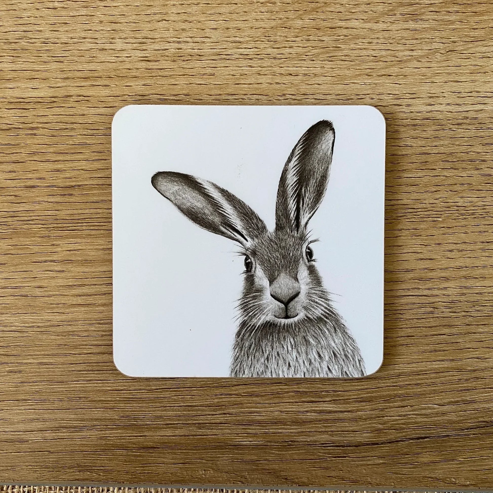 Square white coaster with a printed grayscale image of a hare