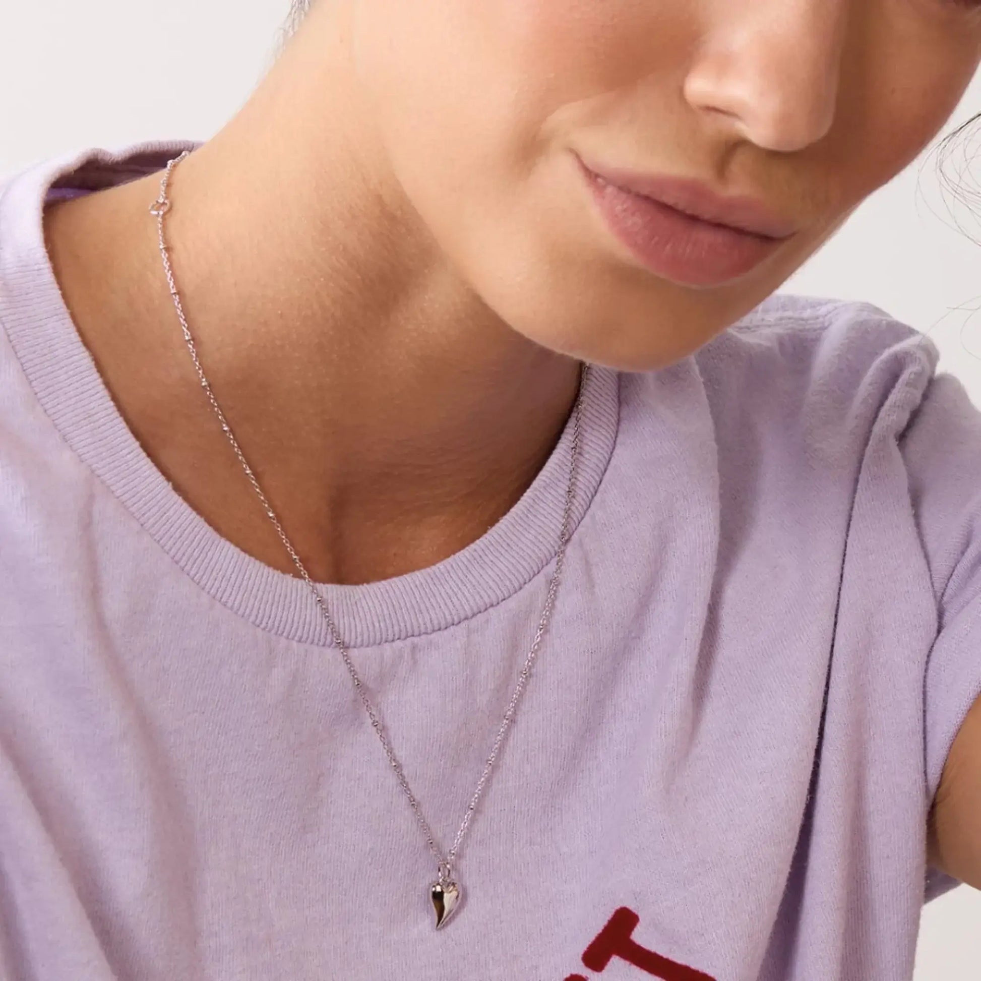 Model wearing a silver asymmetric heart pendant on a silver ball chain 
