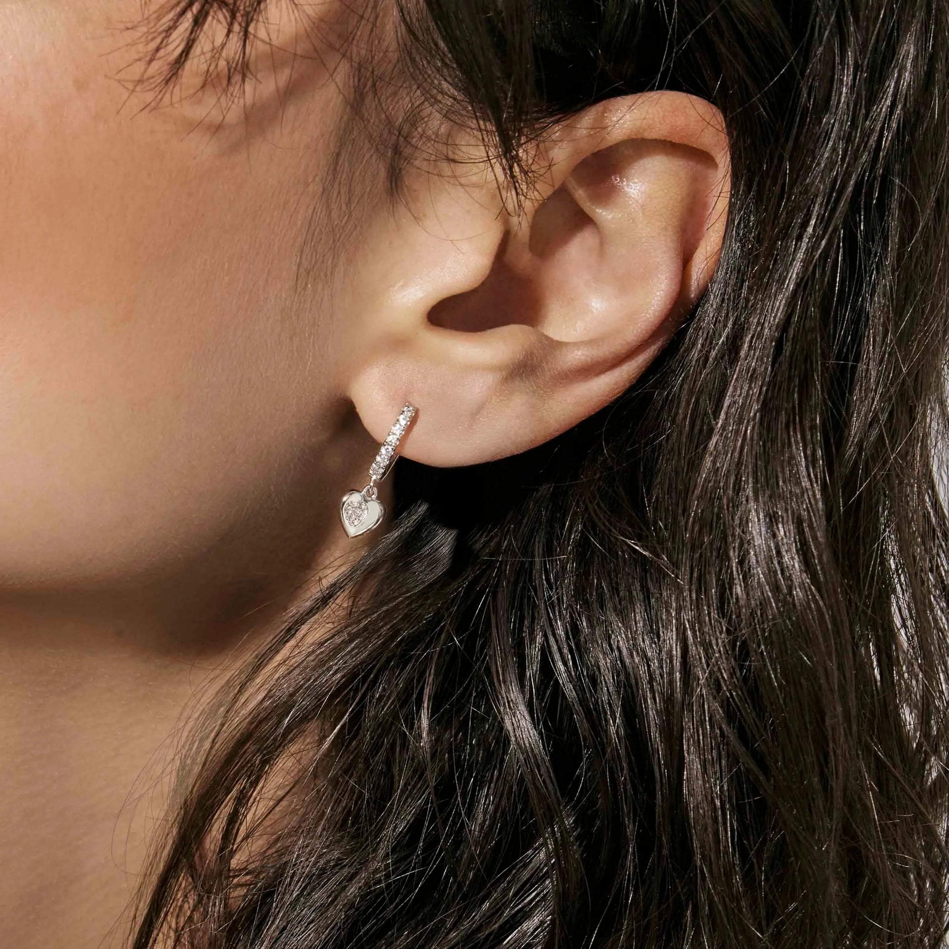 Model wearing Silver hoop earrings featuring heart shaped drop with smaller pave CZ heart cluster inside