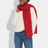 Model wearing a long pink and red blanket scarf featuring a heart pattern and small fringe