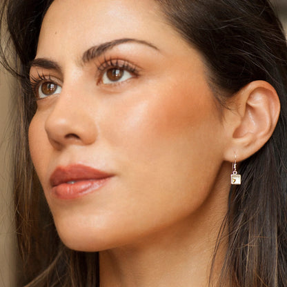 Model wearing silver box shaped drop earrings with tiny gold hearts 