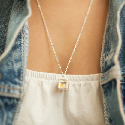 Model wearing silver box shaped pendant with tiny gold heart and silver chain 