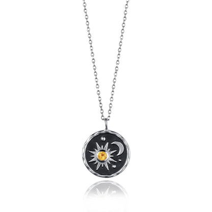 Round coin shaped necklace with black centre and a sun and moon motif set with an orange citrine stone